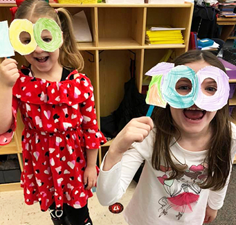 Two spirited elementary girls with 100-day paper eye glasses