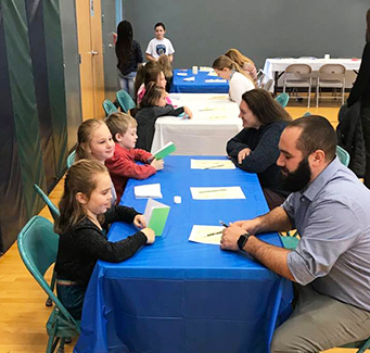 Students and adults sitting at a table during an event